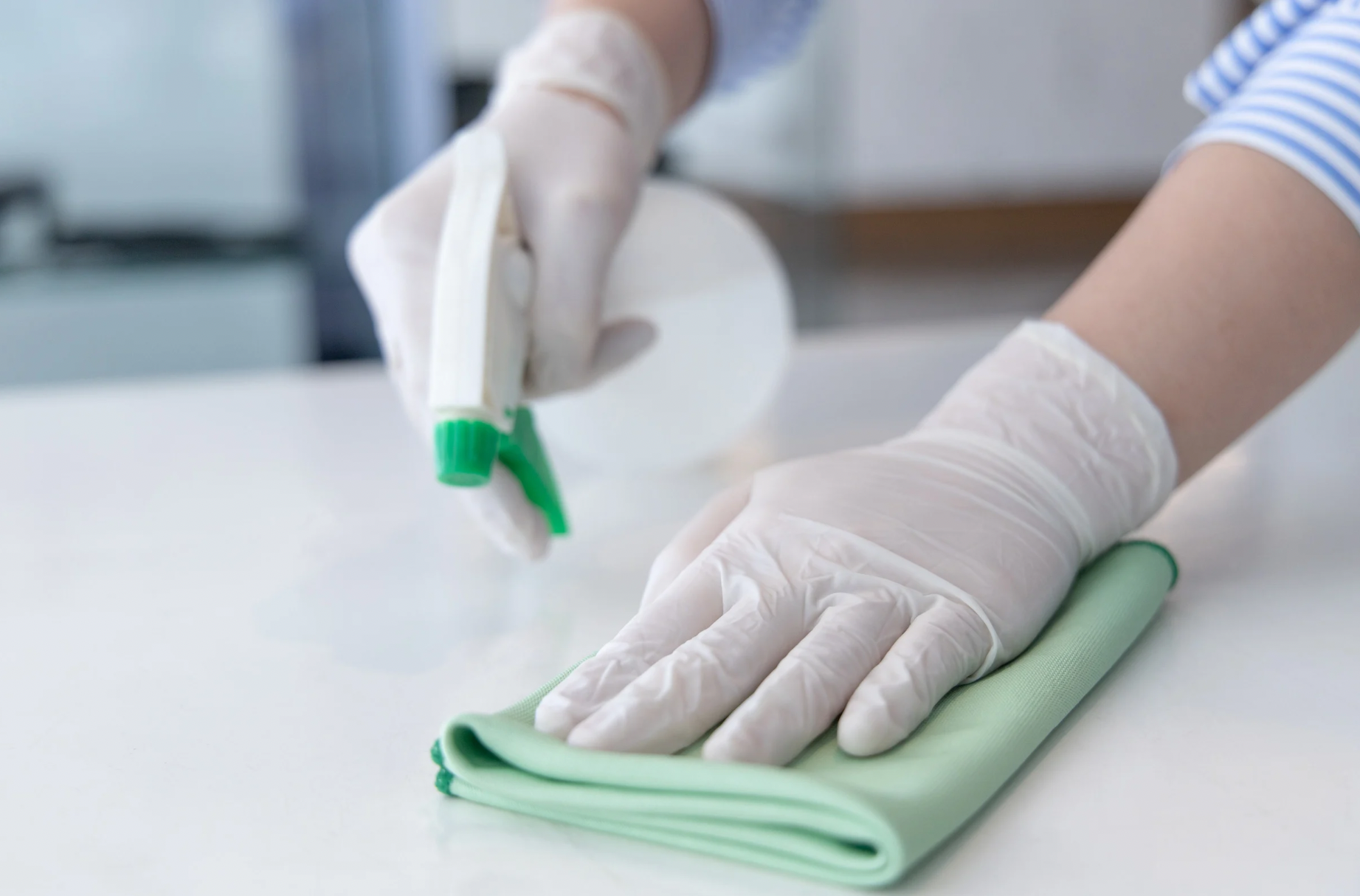 Gloved hands spraying and wiping down a surface with a green cloth